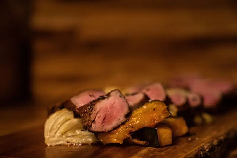 Sliced roasted pork loin over squash on a wooden board